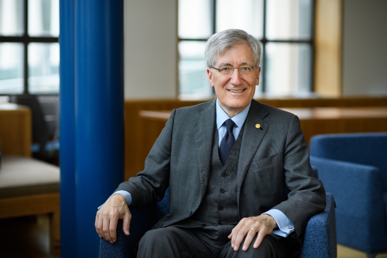 Robert P. George, a gray-haired man wearing glasses and a suit, smiling while seated in a chair in an academic building.