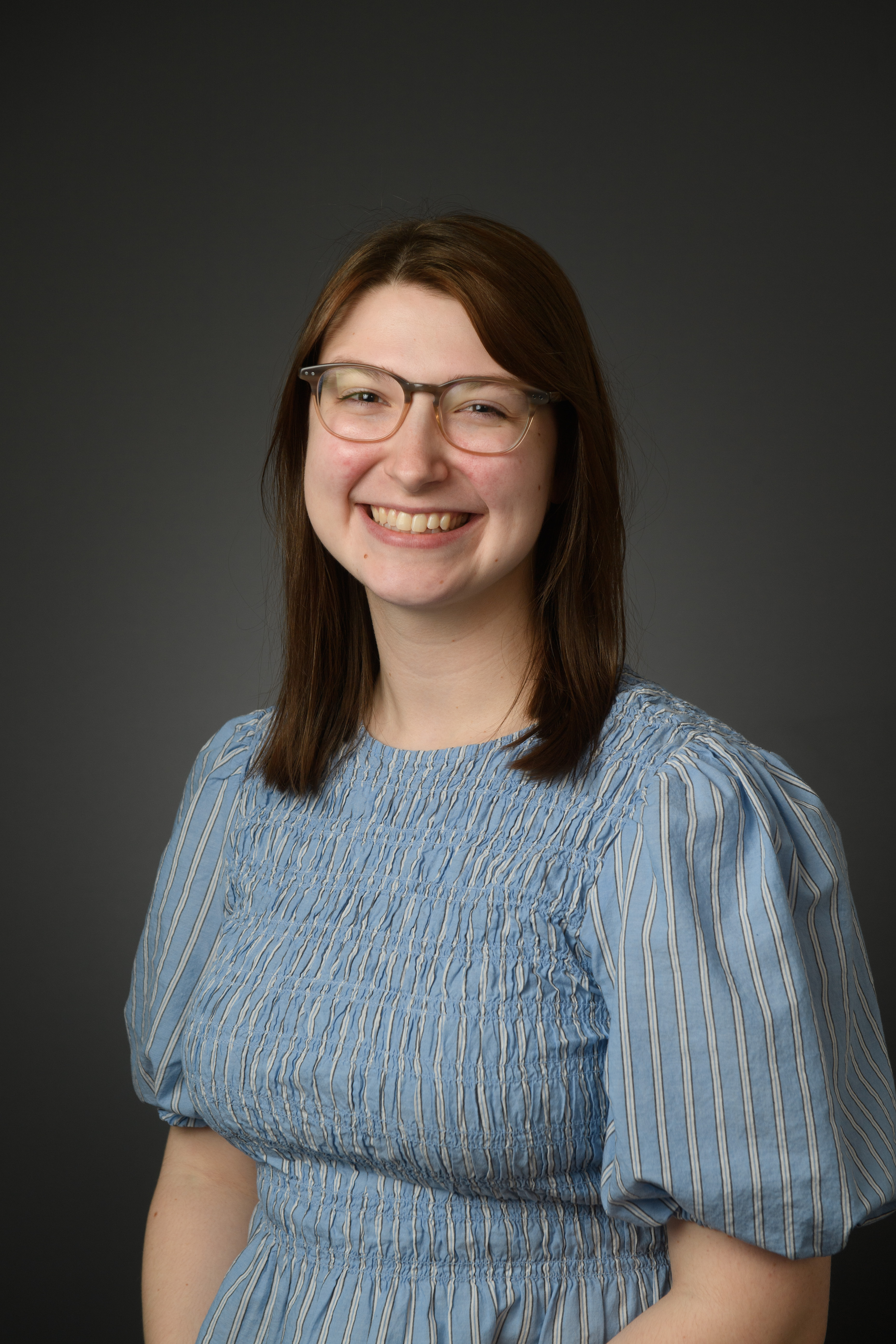 Rachel Williams, a smiling woman with brown hair and glasses wearing a blue shirt against a gray background.