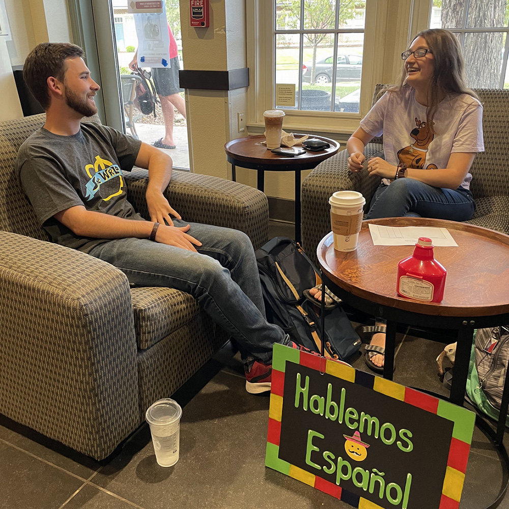 A group of student sit in a circle holding coffee. There are picture frames behind them.