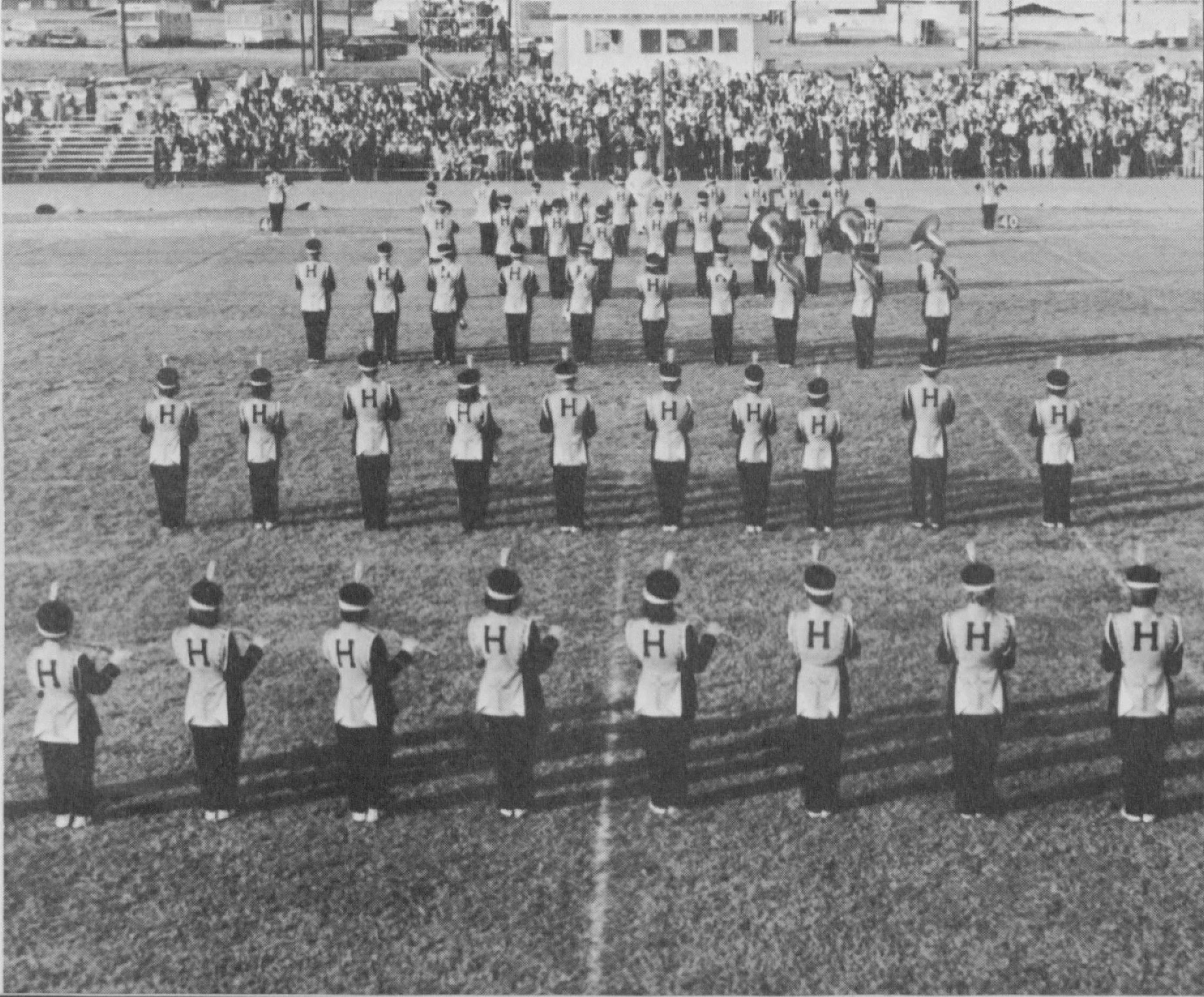 Black and white photo of marching band playing on the Harding football field with a large audience in front of them.