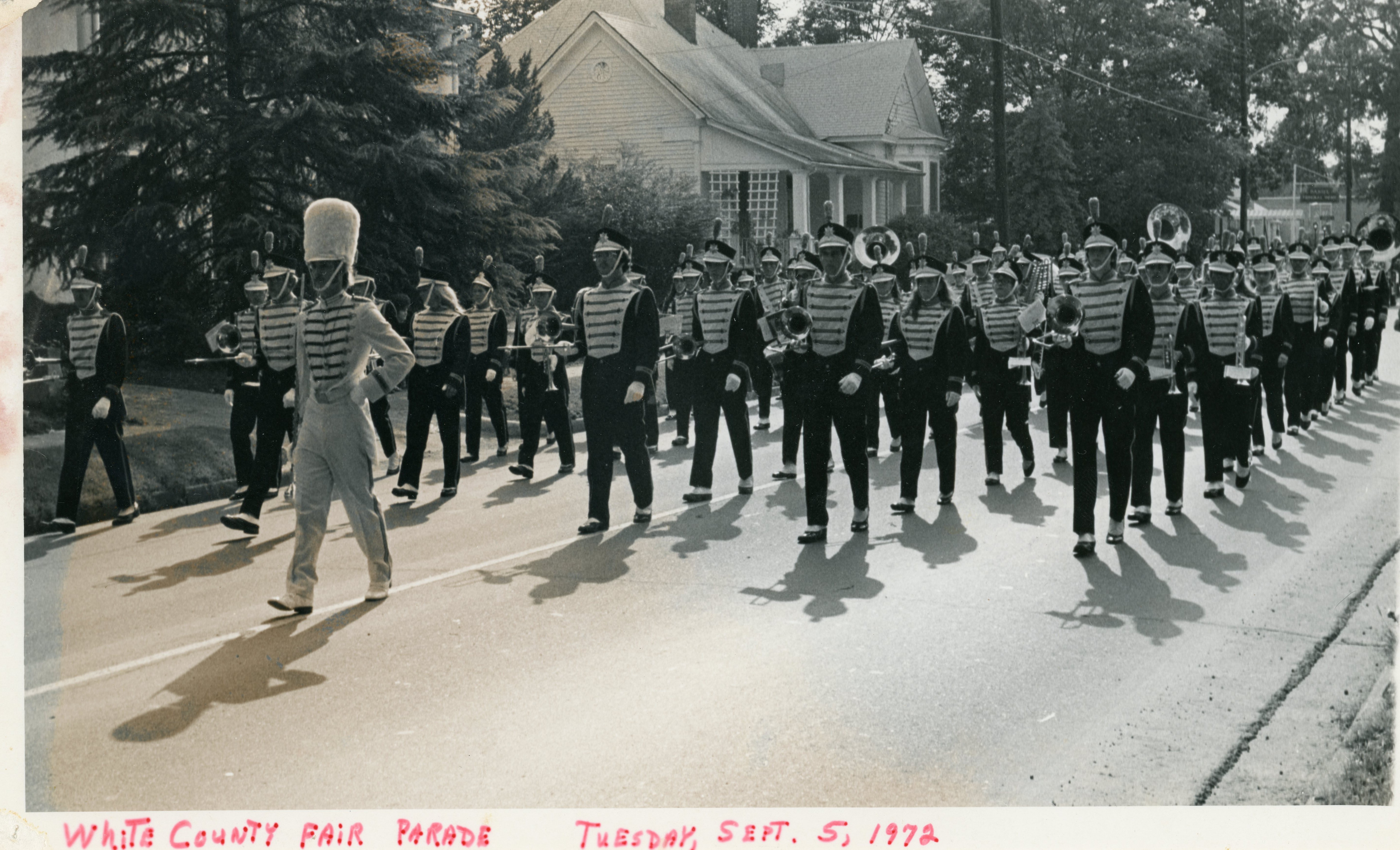 Band marching in formation down a city street dressed in uniforms holding their instruments.