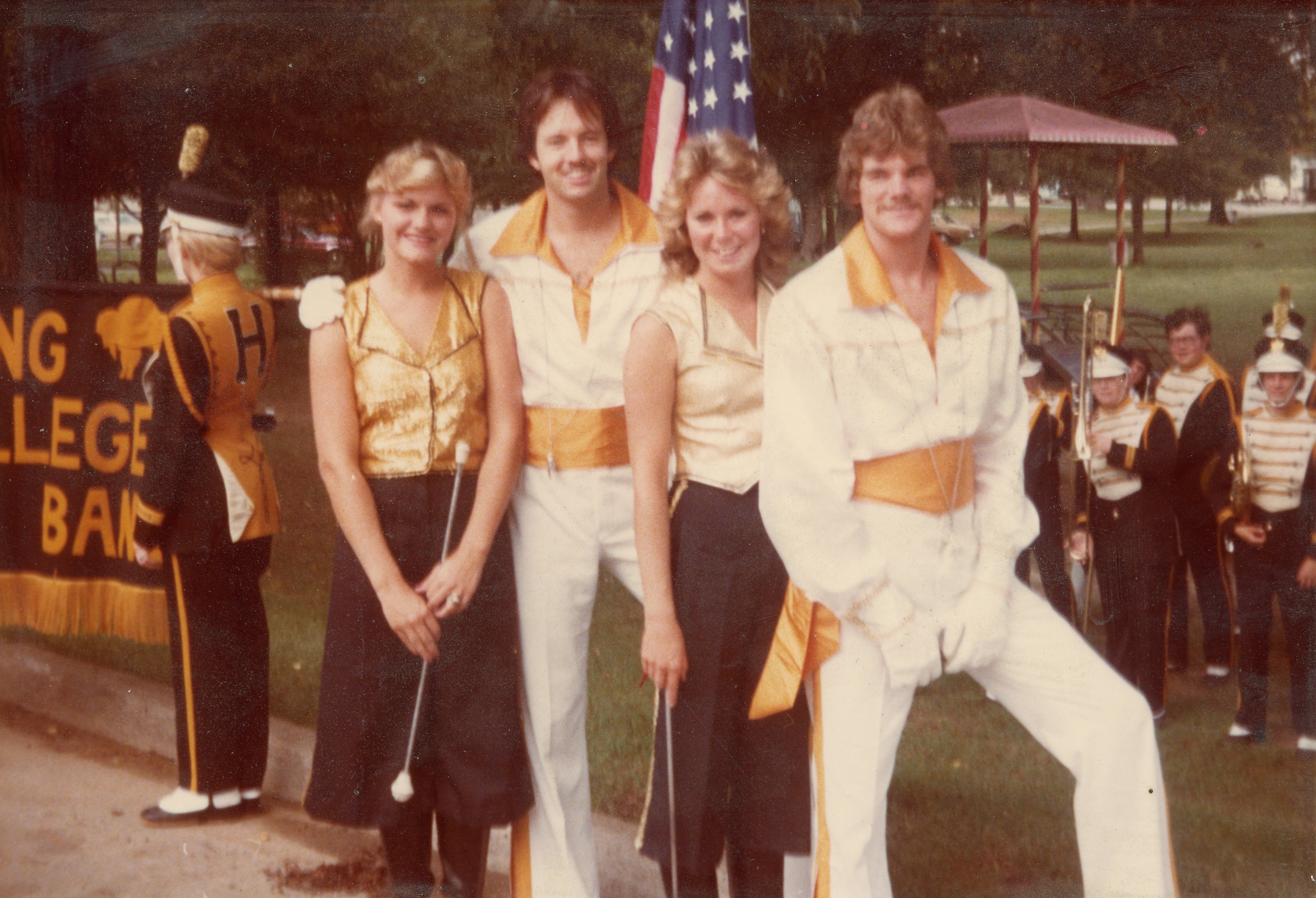 Drum majors and majorettes wearing stylish black, gold, and white uniforms with the band behind them.