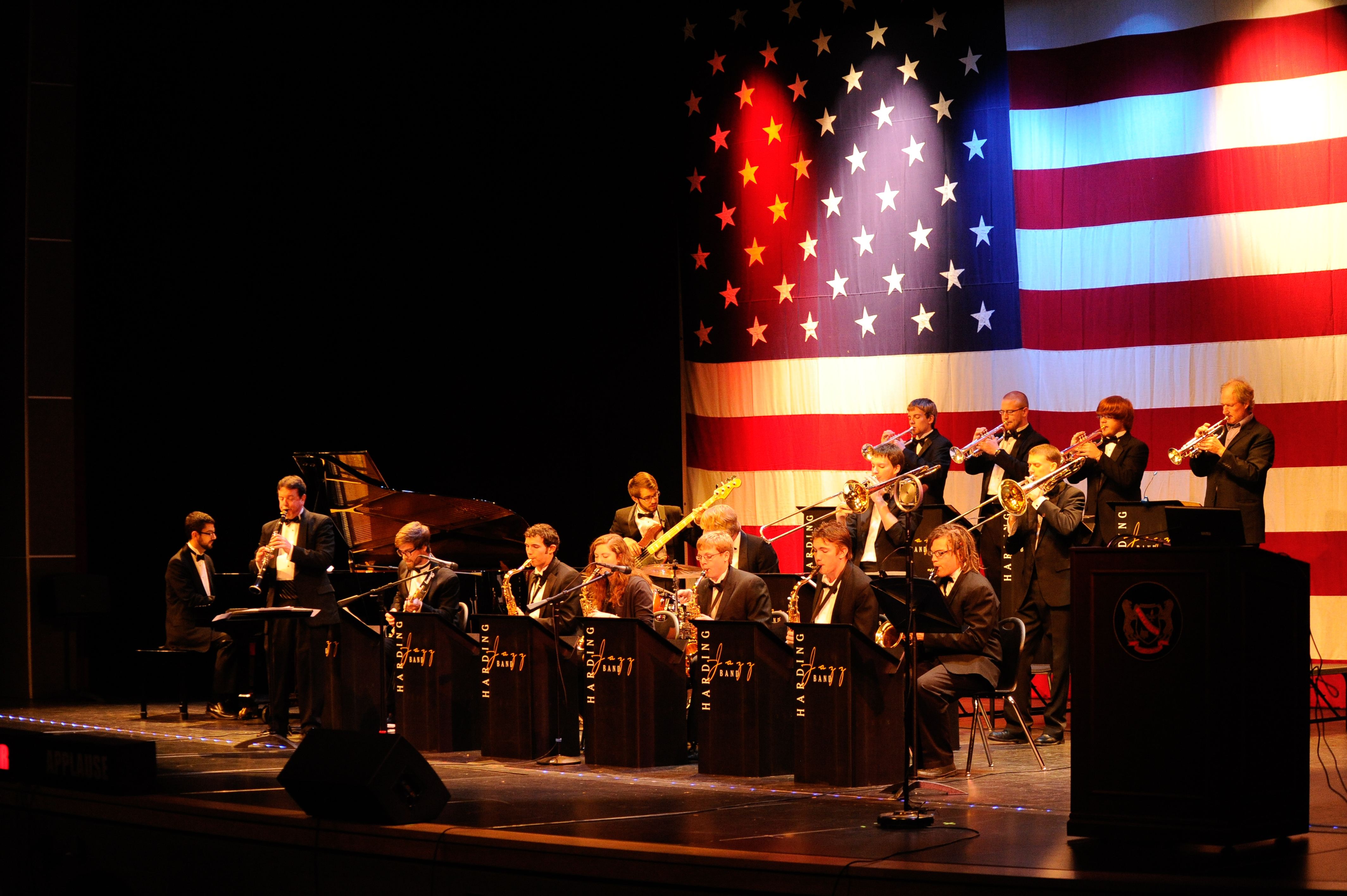 Jazz band on stage performing against a large American flag background with red, white, and blue lighting.