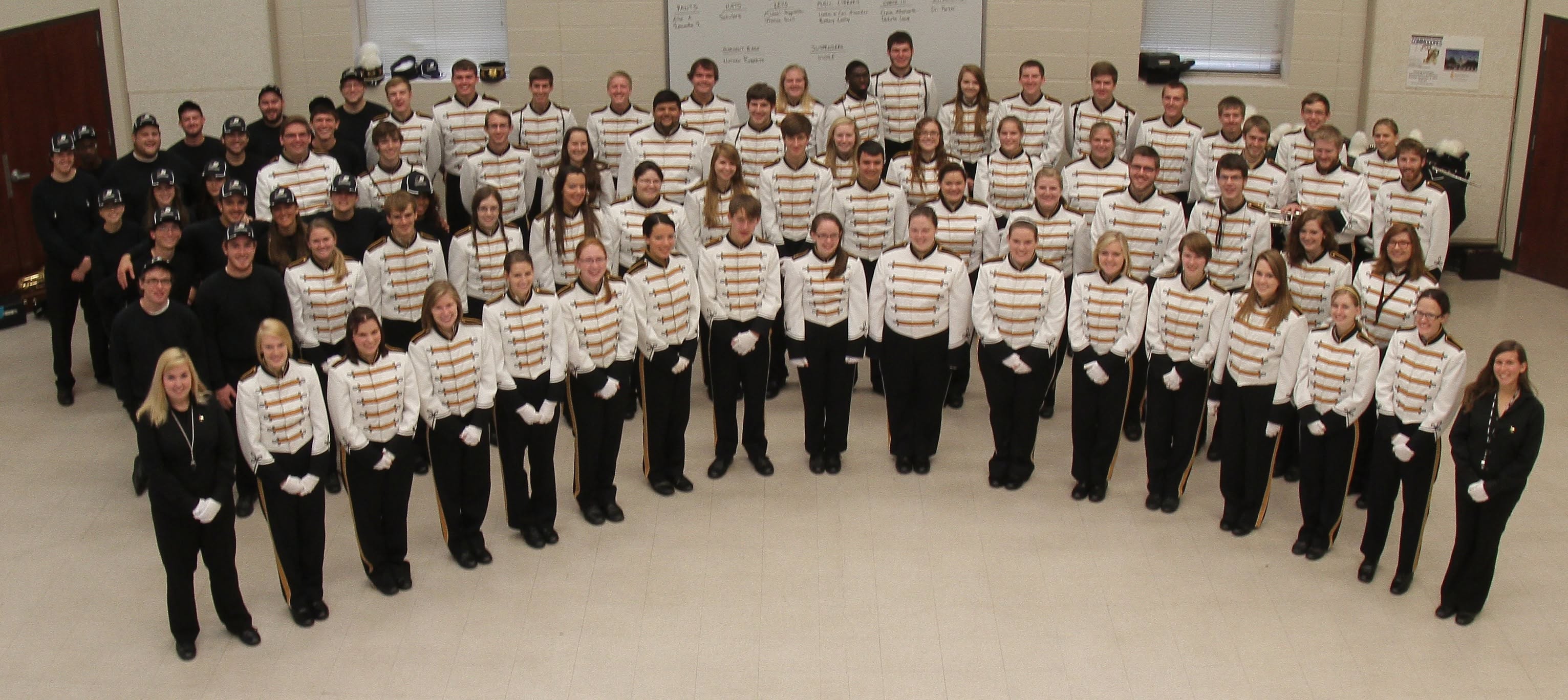 Band standing in a large room wearing black, gold, and white uniforms.