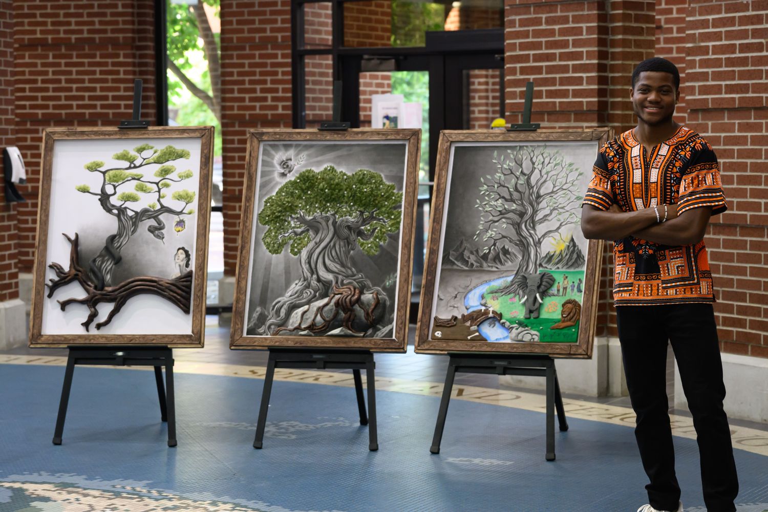 Caledon standing next to his art work of three framed 3 dimentional trees