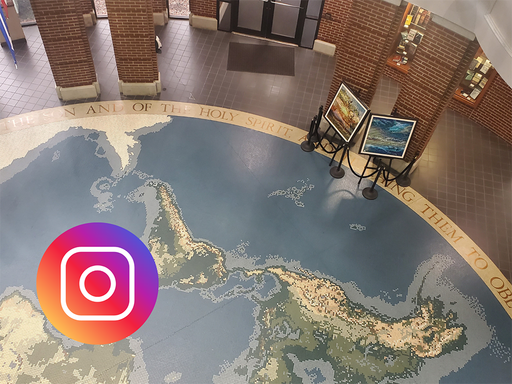 Inside Harding’s McInteer Bible Building with mosaic world map floor, brick columns, and art on display stands.