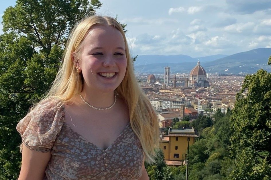 Maggie Samples standing in front of the with a European city behind
