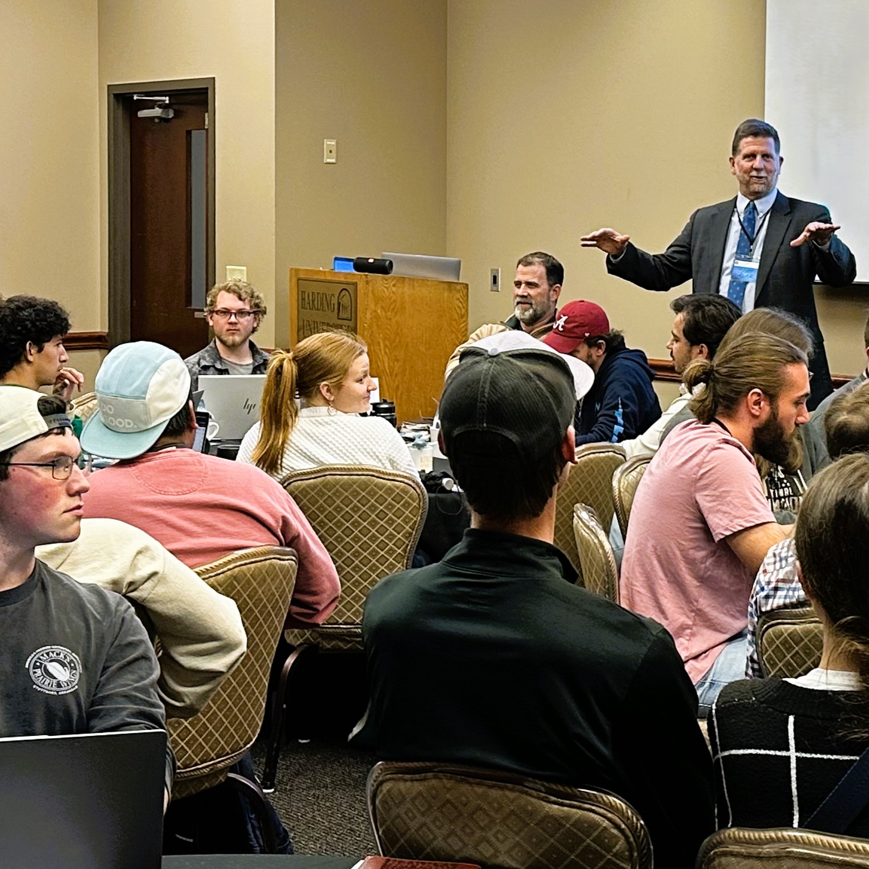 Dr. Scott Adair, a man in a suit, standing up speaking to an audience of youth ministers at the Youth Ministry Workshop.
