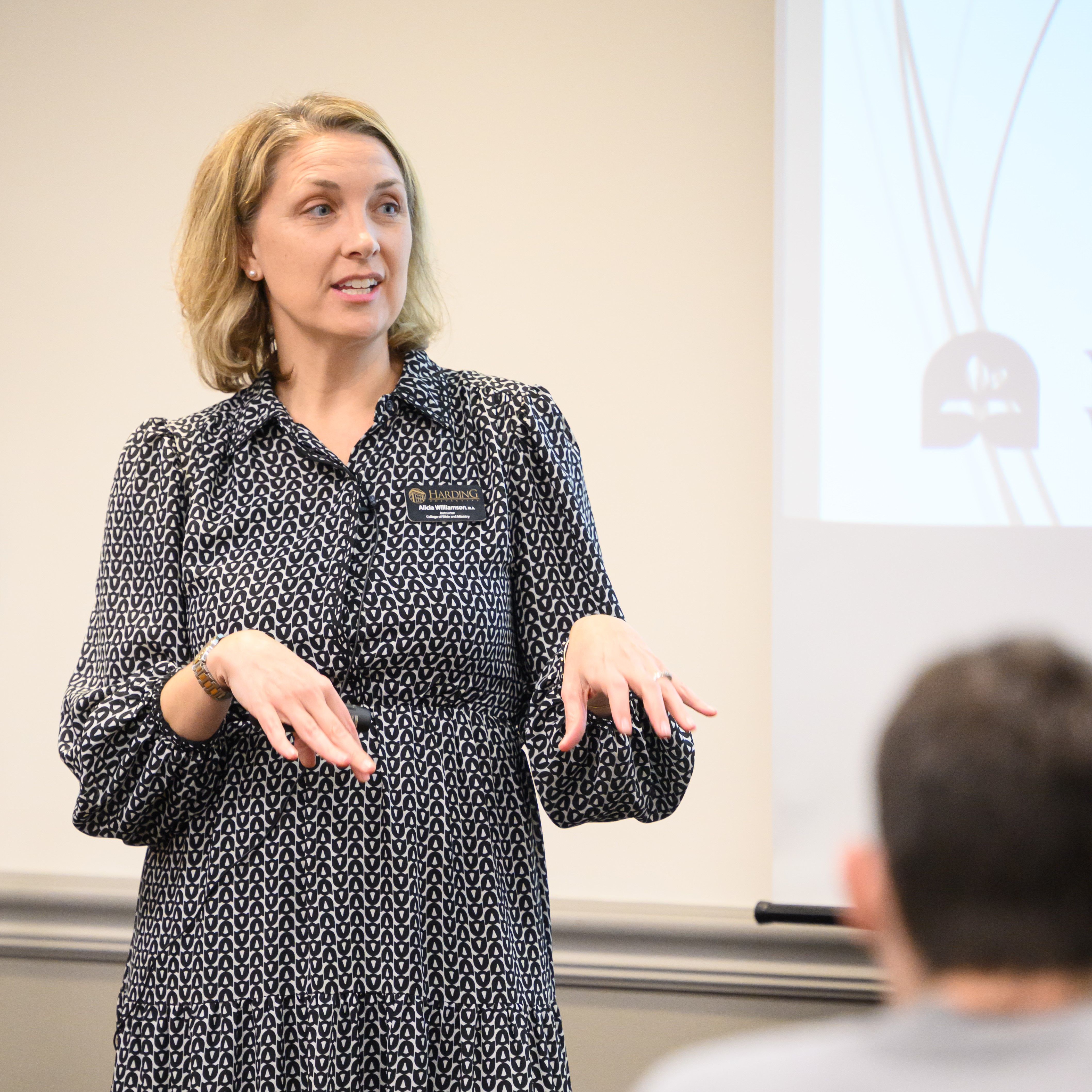 Dr Alicia Williamson, a woman in a dress, standing up speaking to an audience of youth ministers at the Youth Ministry Workshop.