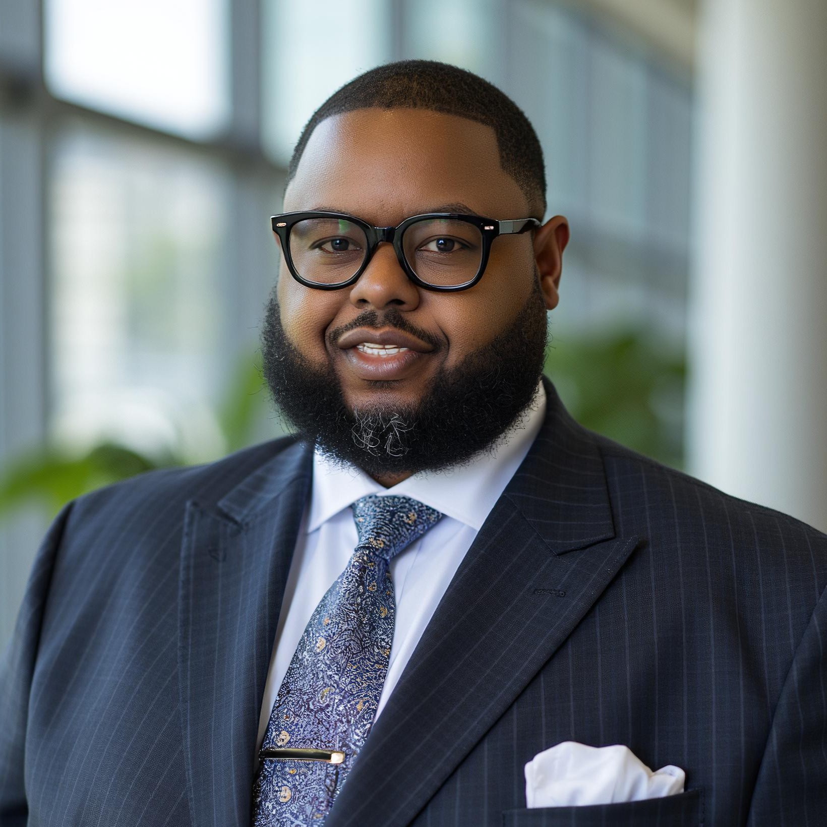 Dr. Anwar Carter smiles in glasses in a black suit