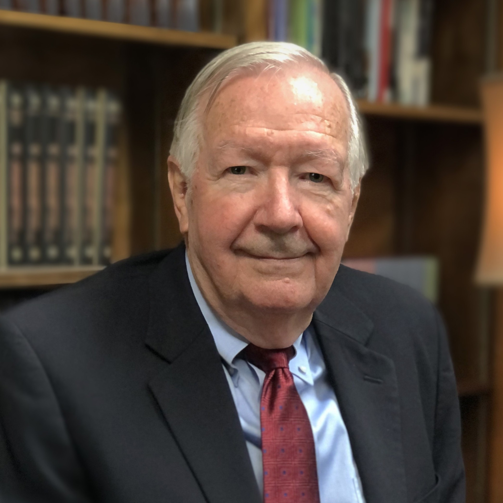 Dr. James Thompson in a suit sits in an arm chair in front of a book shelf