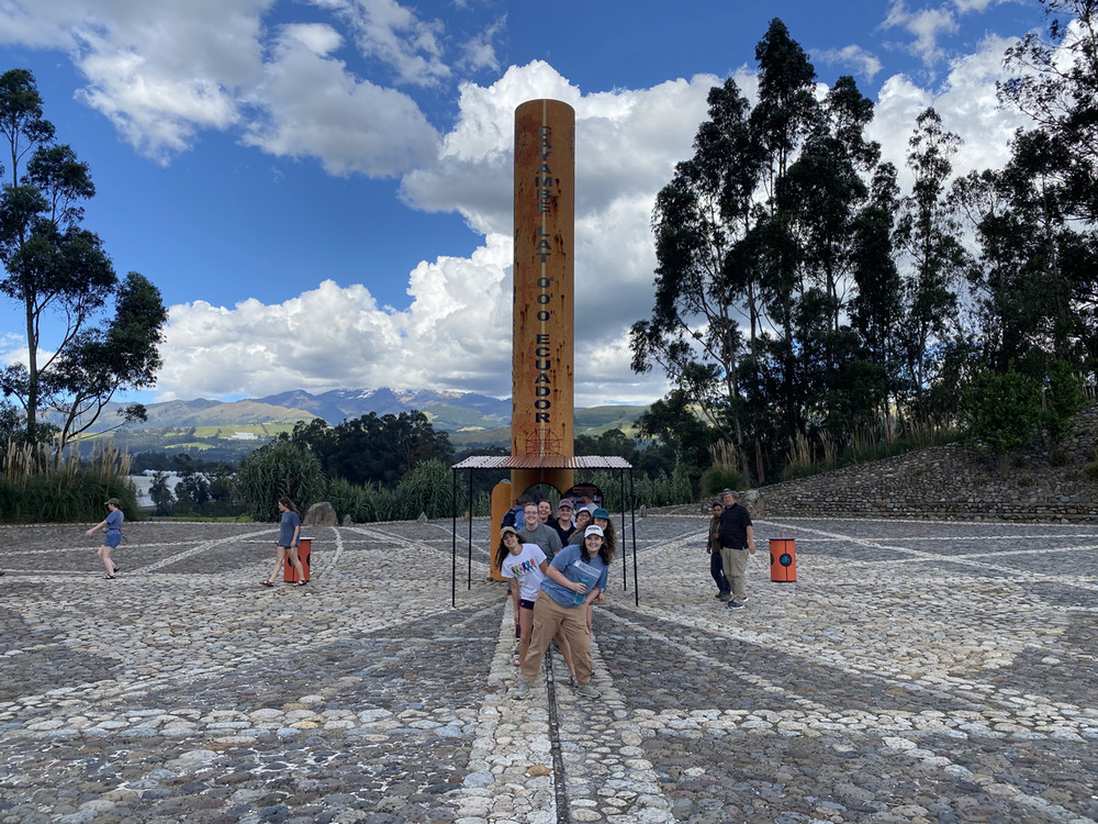 Interns pose in front of wooden pillar in the center of a stone ring