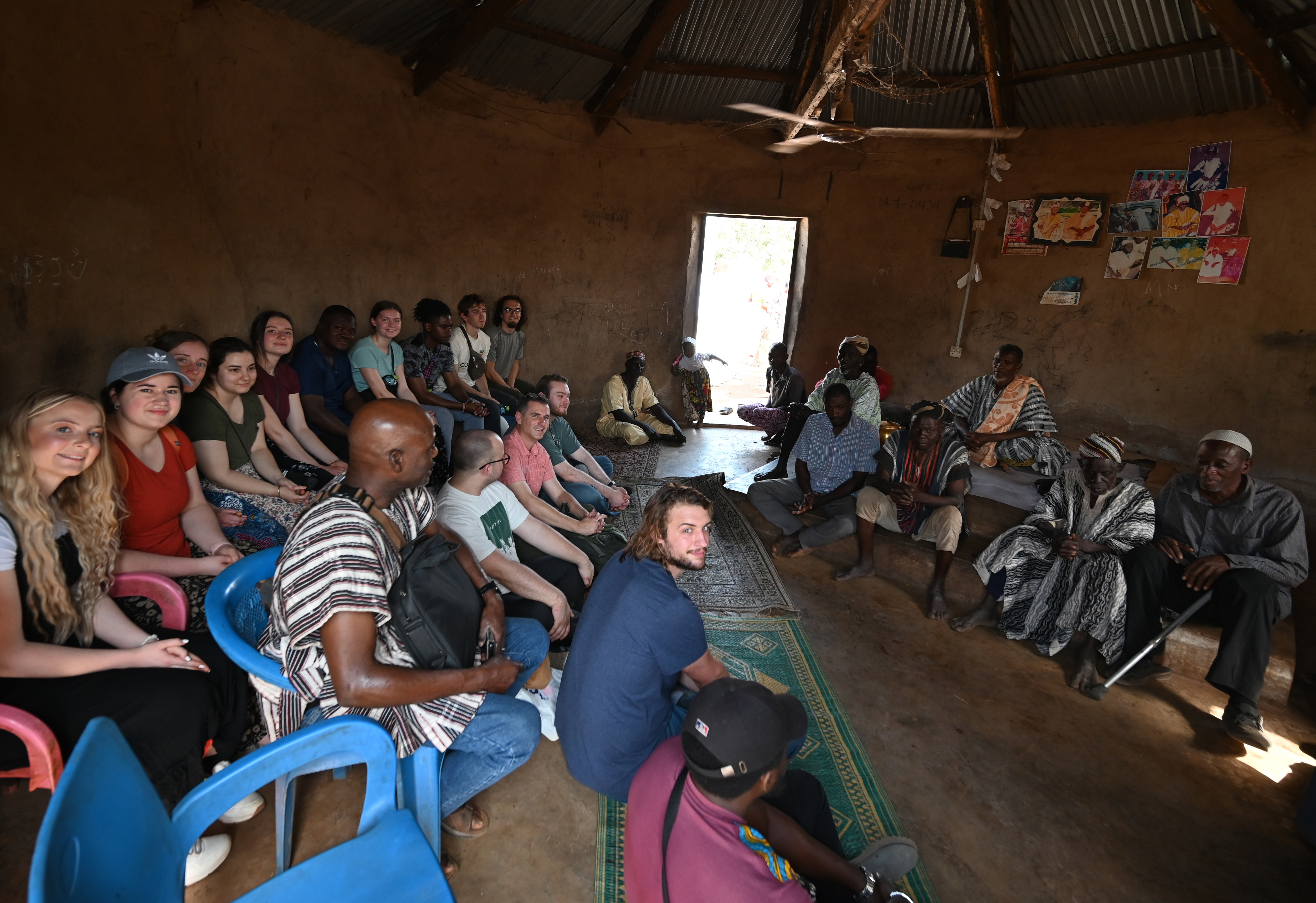 Group of people listening to a speaker in a mud hut.