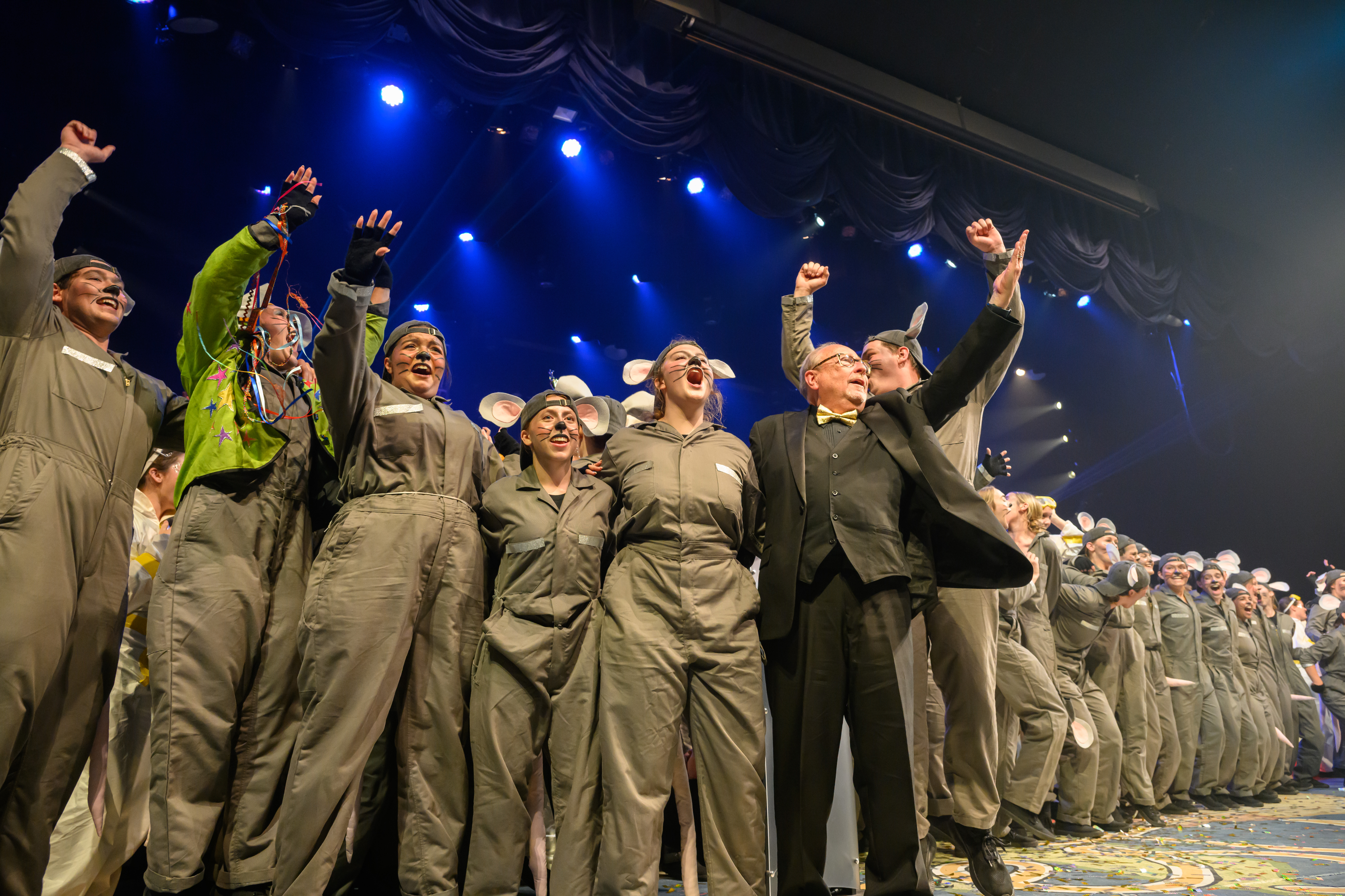 Members of sweepstakes award winner The City That Never Squeaks jumping and celebrating on stage with Spring Sing director Steven Frye.