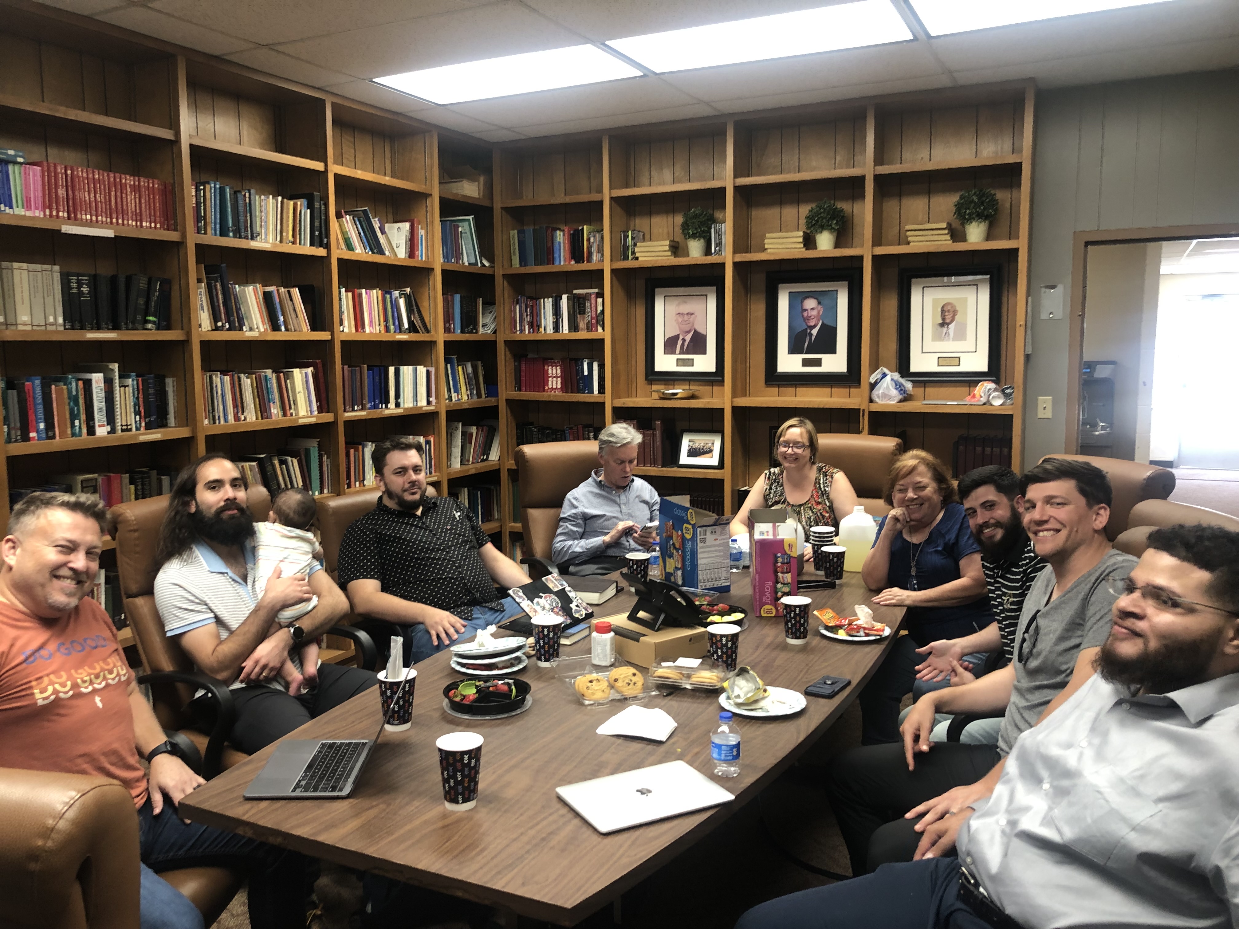 Group of people in the church classroom sitting around a table smiling.