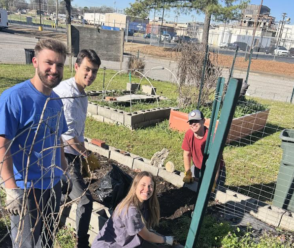 A group of four people gardening together in a community garden, smiling and working in raised beds.