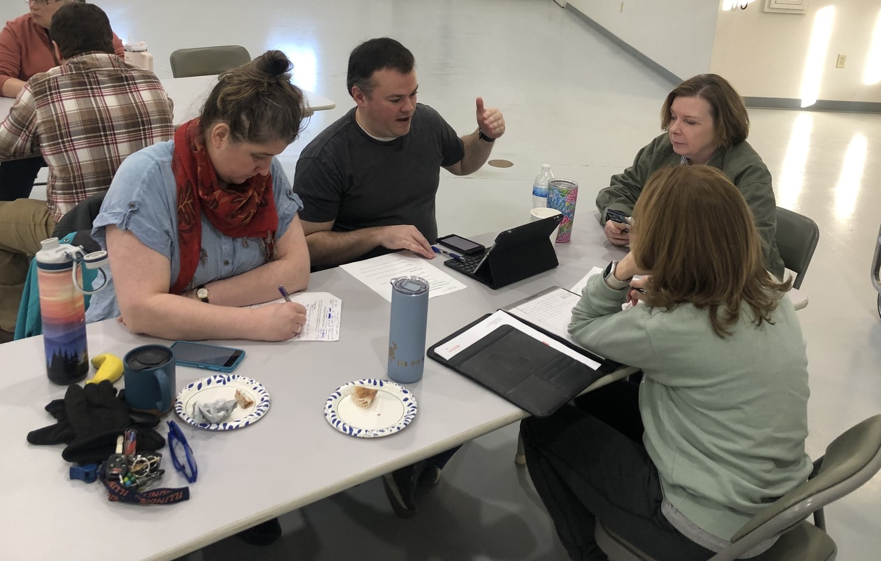 Groups of people gathered around tables talking and taking notes.