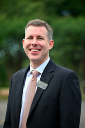 Dr. Steve Cloer smiling in a suit, posed in front of a blurred outdoor background.