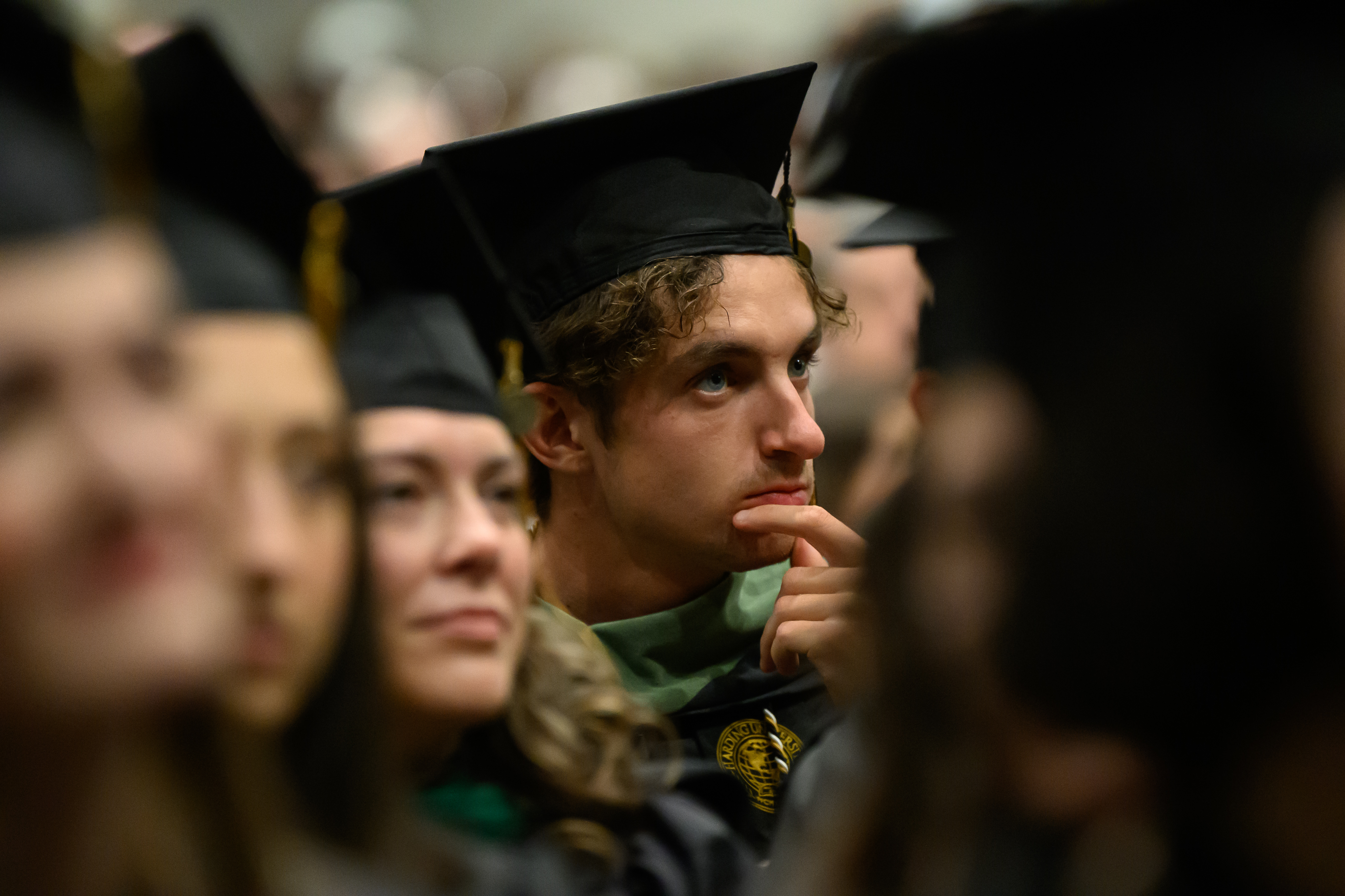 Young male graduate holds his chin at graduation, contemplating his future.