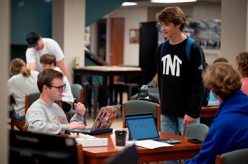 Three students are gathered around a table talking. They are wearing club sweatshirts.
