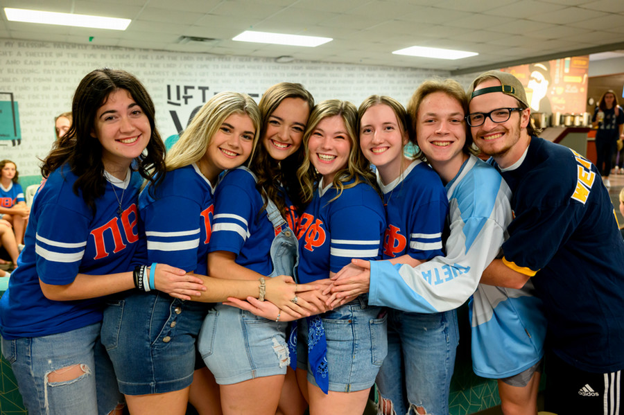 Students wearing Pi Theta Phi and Gamma Sigma Phi Jerseys hugging for a group photo.