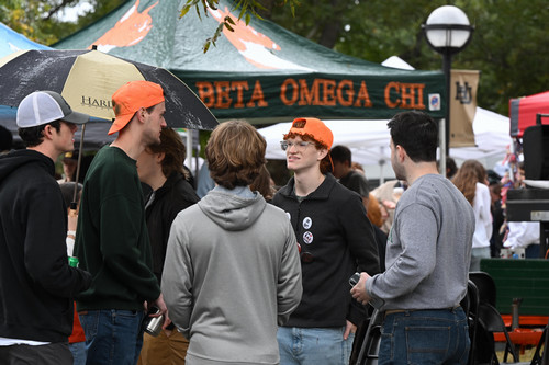 Members of Beta Omega Chi talking in a group during a football tailgate on a rainy day.