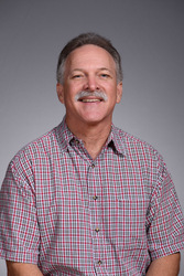 Dr. J.D. Yingling wearing a red and gray plaid shirt, smiling in front of a neutral gray background.