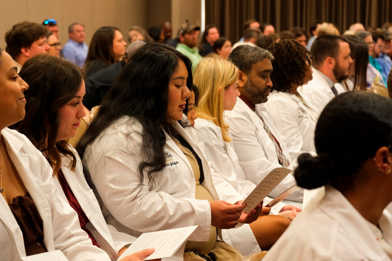 Incoming pharmacy students sitting at their white coat ceremony while reading programs